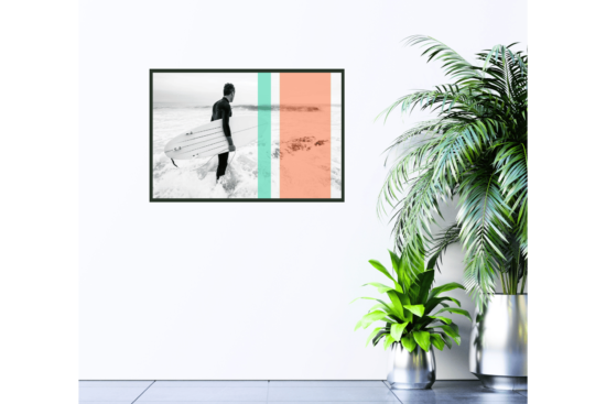 Black and white of surfer on beach holding surfboard with orange and teal stripe overlays picture hanging on wall